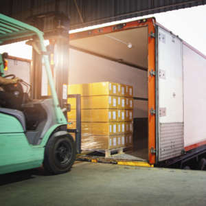 A green forklift is placing a shrink-wrapped pallet of carton stock into the back of a trailer