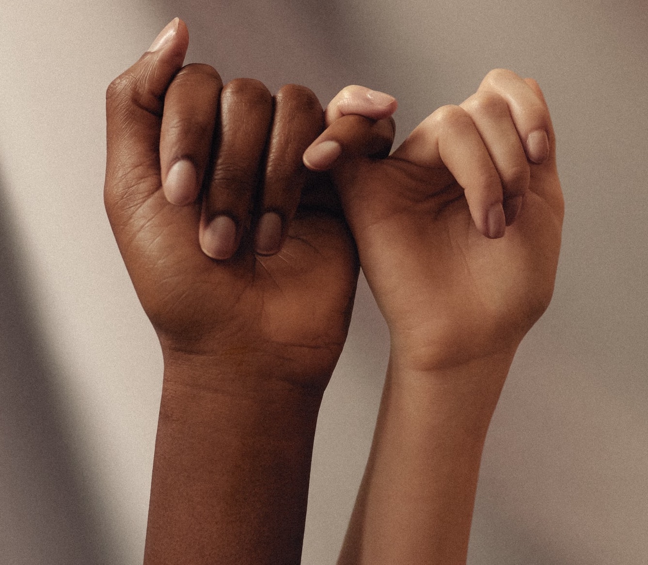 Two hands of different races pinky promise to represent solidarity and support within a workplace